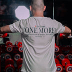 A man lifting weights with a white shirt on displaying motivational text with Zechariah 4:6, in a gym setting