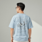 Person wearing a light blue t-shirt with text and a graphic on the back, standing against a plain background.