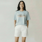 Woman wearing a light blue t-shirt with a graphic design and white shorts on a plain background