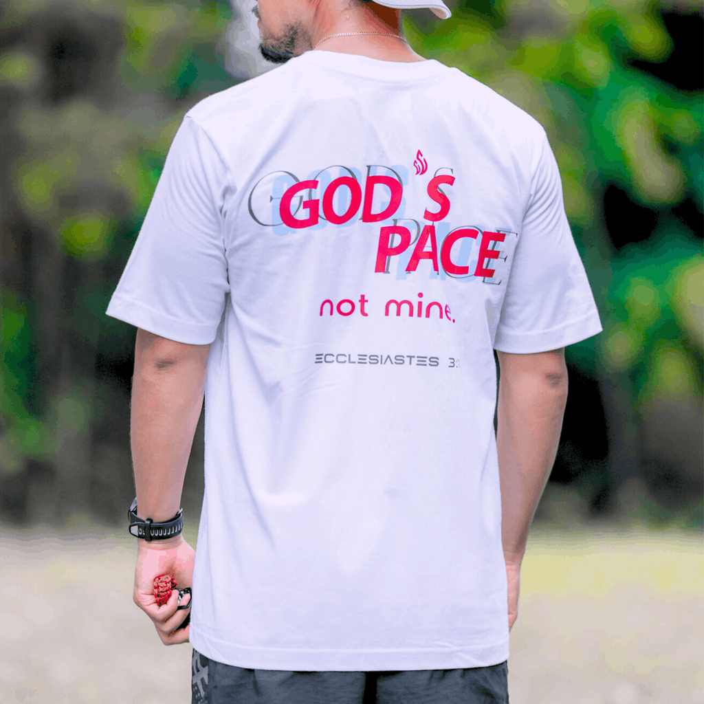 Person wearing a white t-shirt with text that says 'GOD'S PACE not mine.' and 'Ecclesiastes 3:11' below, standing outdoors