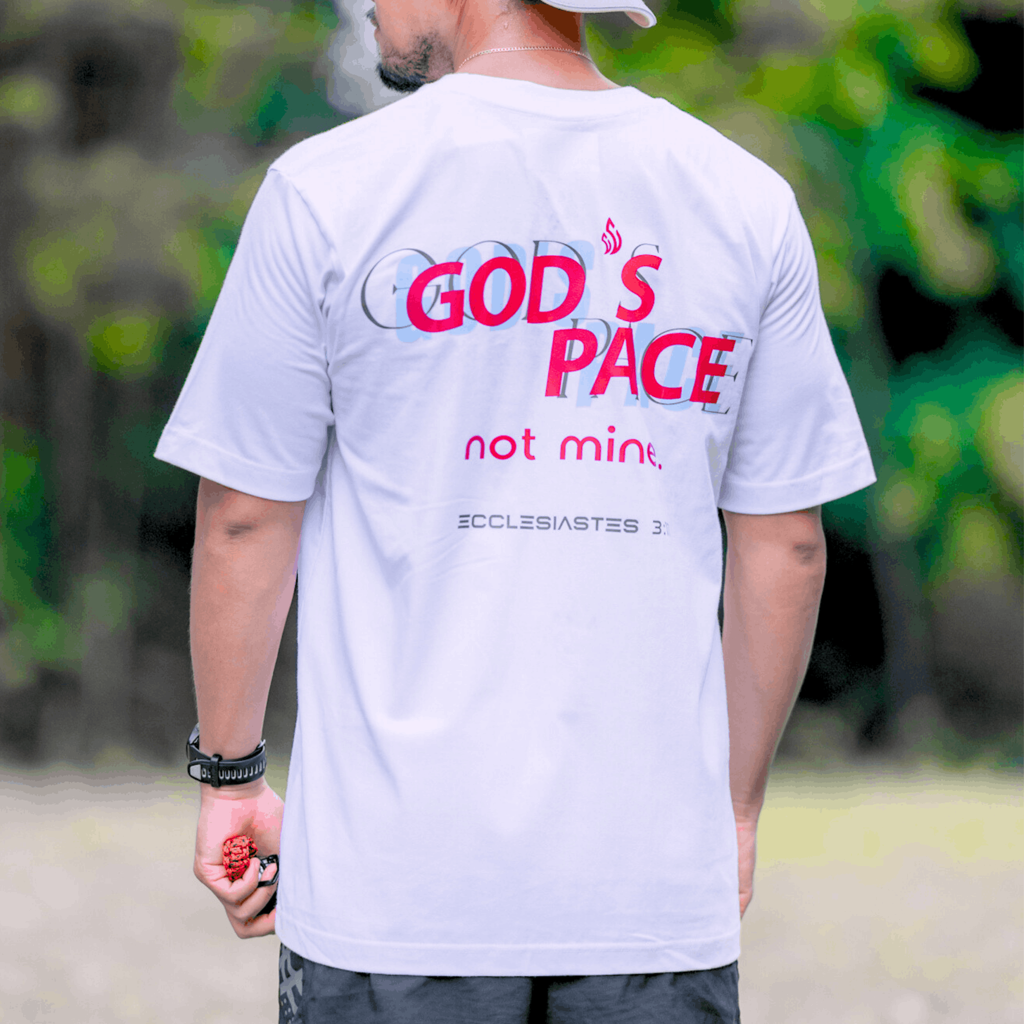 Person wearing a white t-shirt with text that says 'GOD'S PACE not mine.' and 'Ecclesiastes 3:11' below, standing outdoors