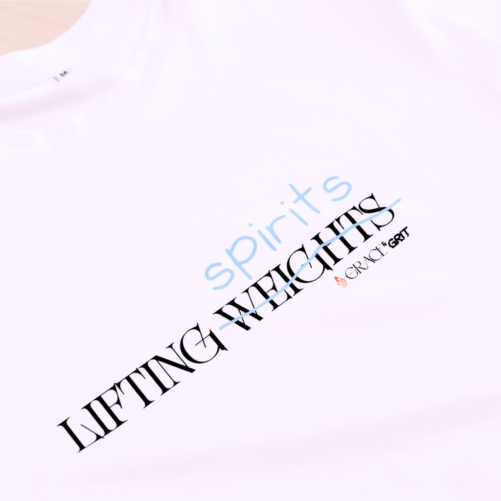 White t-shirt with a print that says 'LIFTING spirits 𝖶̶𝖤̶𝖨̶𝖦̶𝖧̶𝖳̶𝖲̶' 