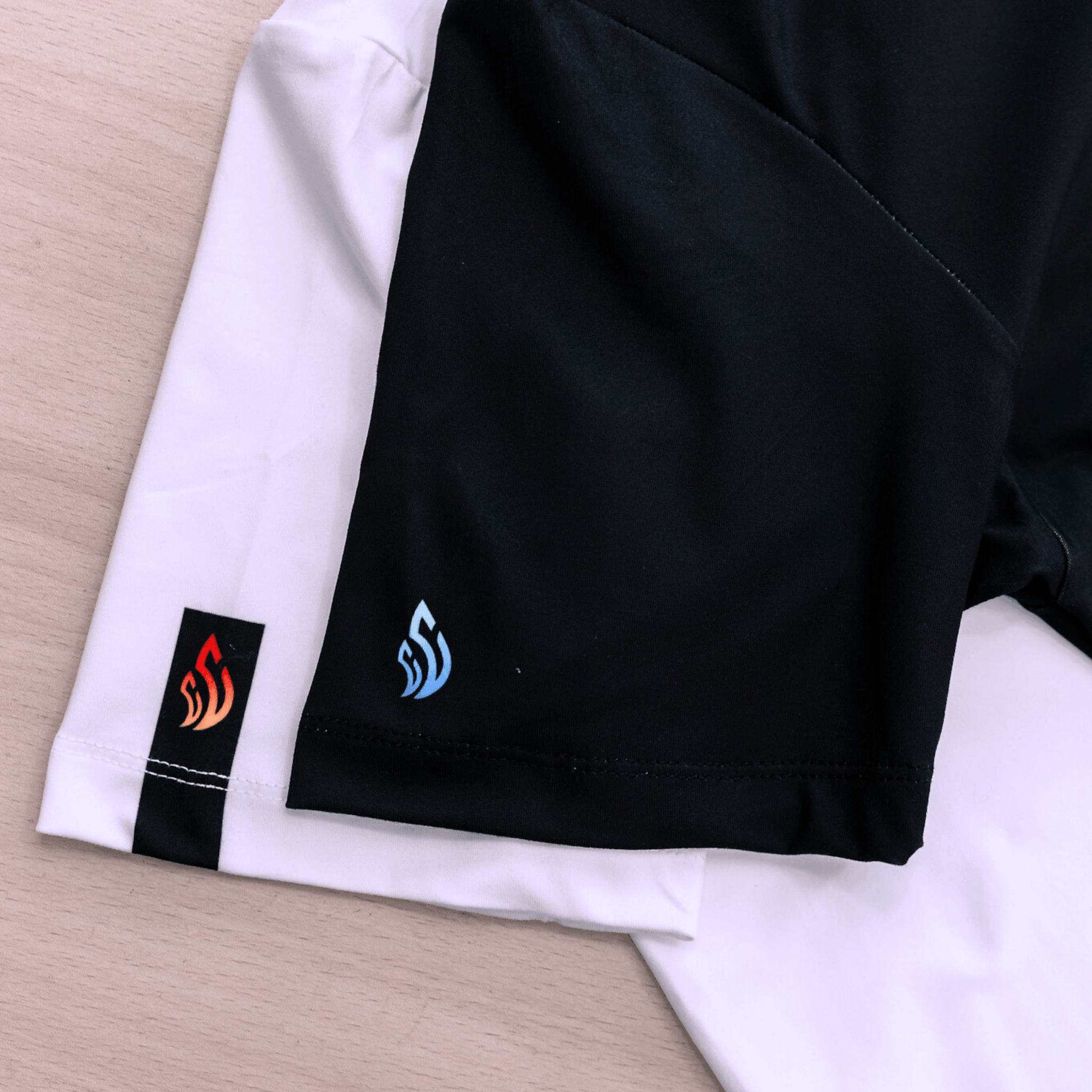 Close-up of a black and white t-shirt with logos on their sleeve, on a wooden surface