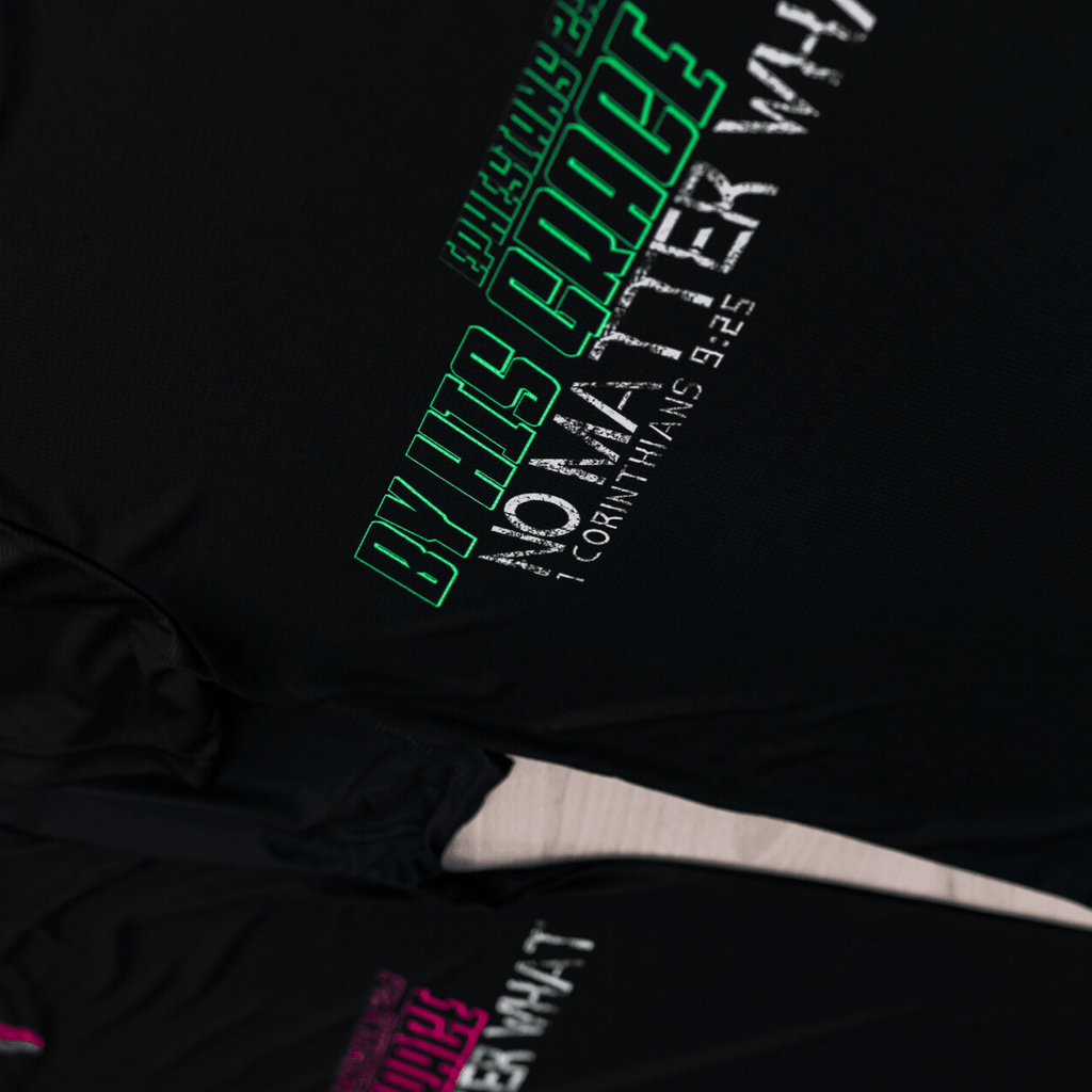 Two black running shirts with vibrant colored text that says 'Ephesians 2:8. By His grace No Matter What. 1 Corintians 9:25. Both the Mint and Black and Pink and Black variants are visible