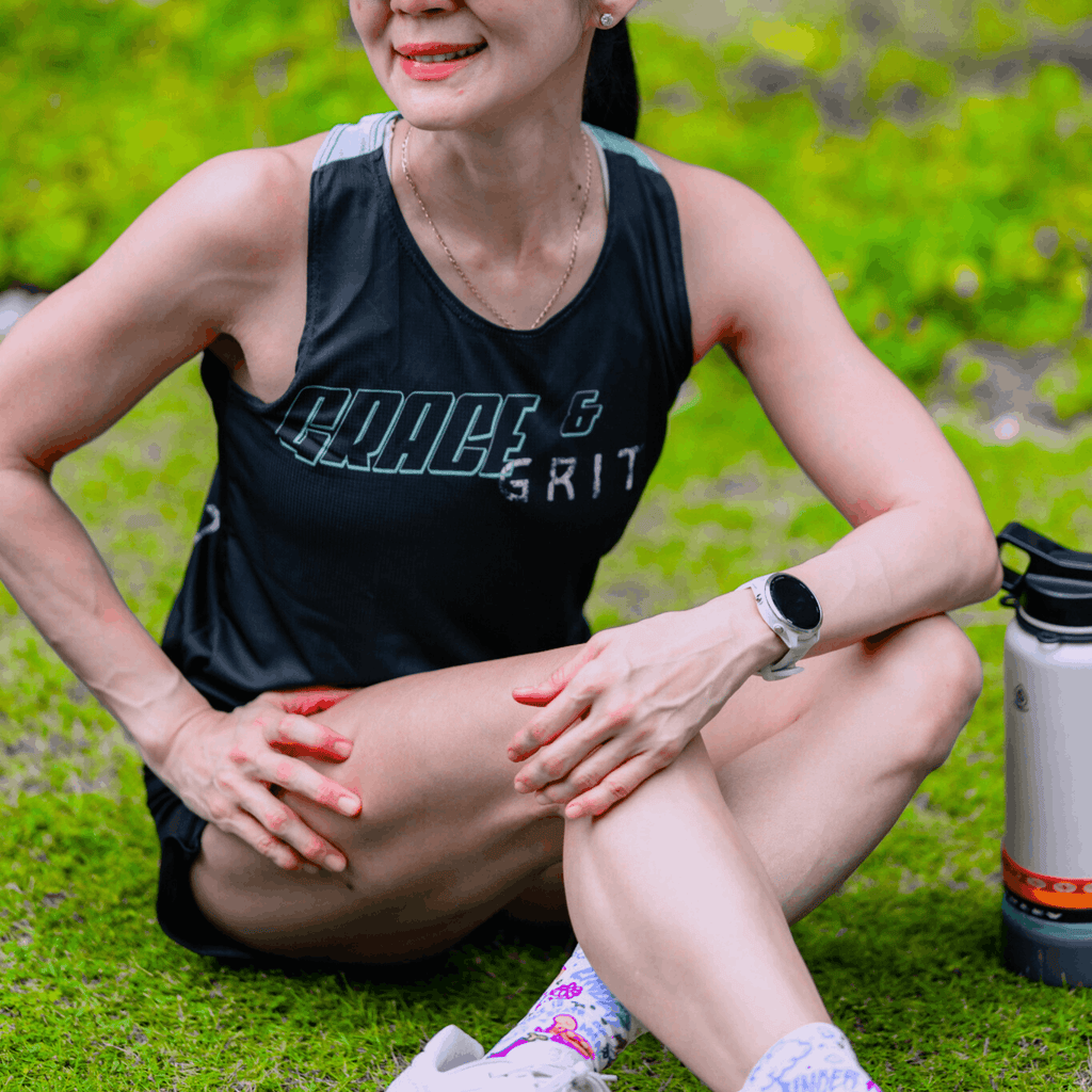 A woman wearing mint and black running singlet and sitting on the ground next to water bottle