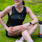 A woman wearing mint and black running singlet and sitting on the ground next to water bottle