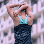 A gentleman stretching outdoors wearing a mint and black singlet, facing away from camera and wearing a cap.