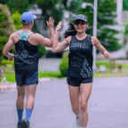 Two runners high-fiving each other on a road, both wearing the mint and black running signet with green and white text.