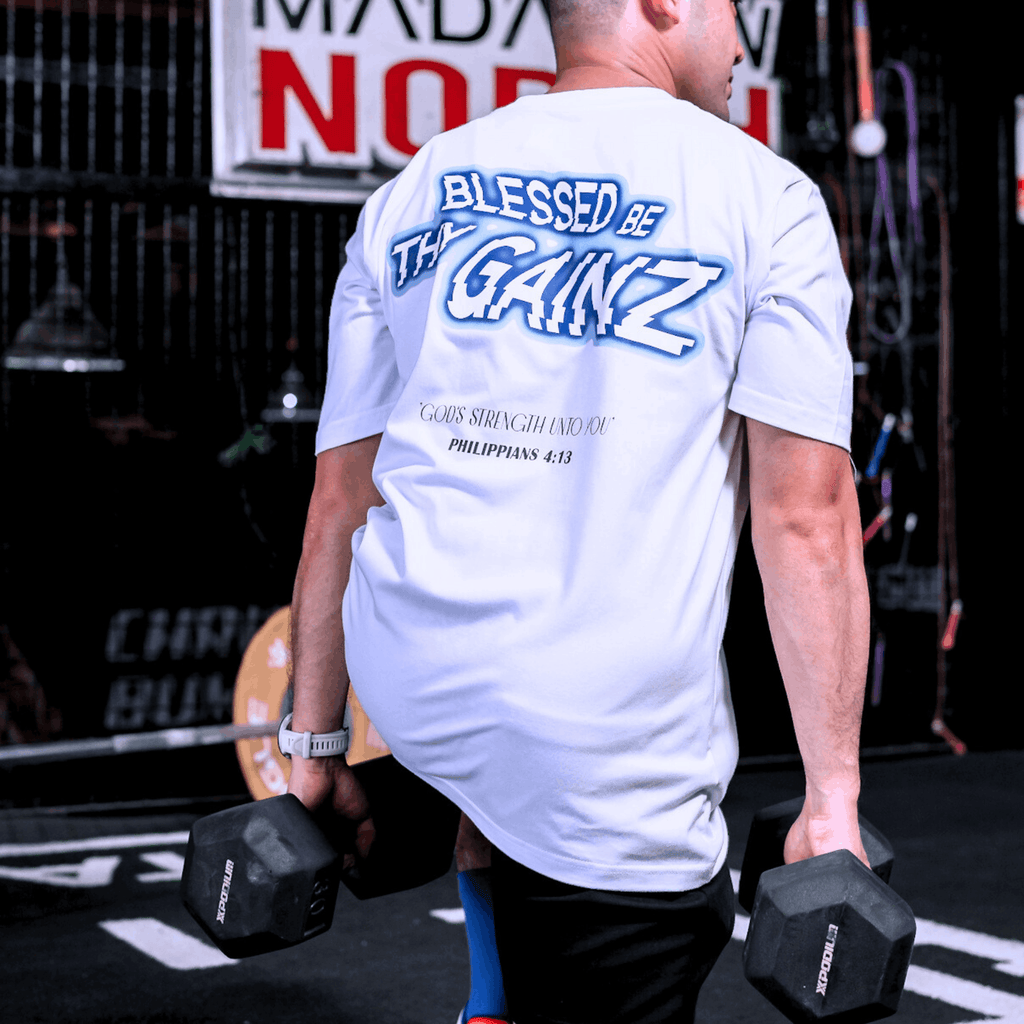 A person wearing a white t-shirt with a  print that says 'BLESSED BE THY GAINZ' and "'GOD'S STRENGTH UNTO YOU' PHILIPPIANS 4:13" while lifting dumbbells