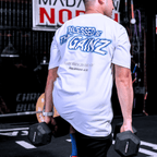 A person wearing a white t-shirt with a  print that says 'BLESSED BE THY GAINZ' and "'GOD'S STRENGTH UNTO YOU' PHILIPPIANS 4:13" while lifting dumbbells